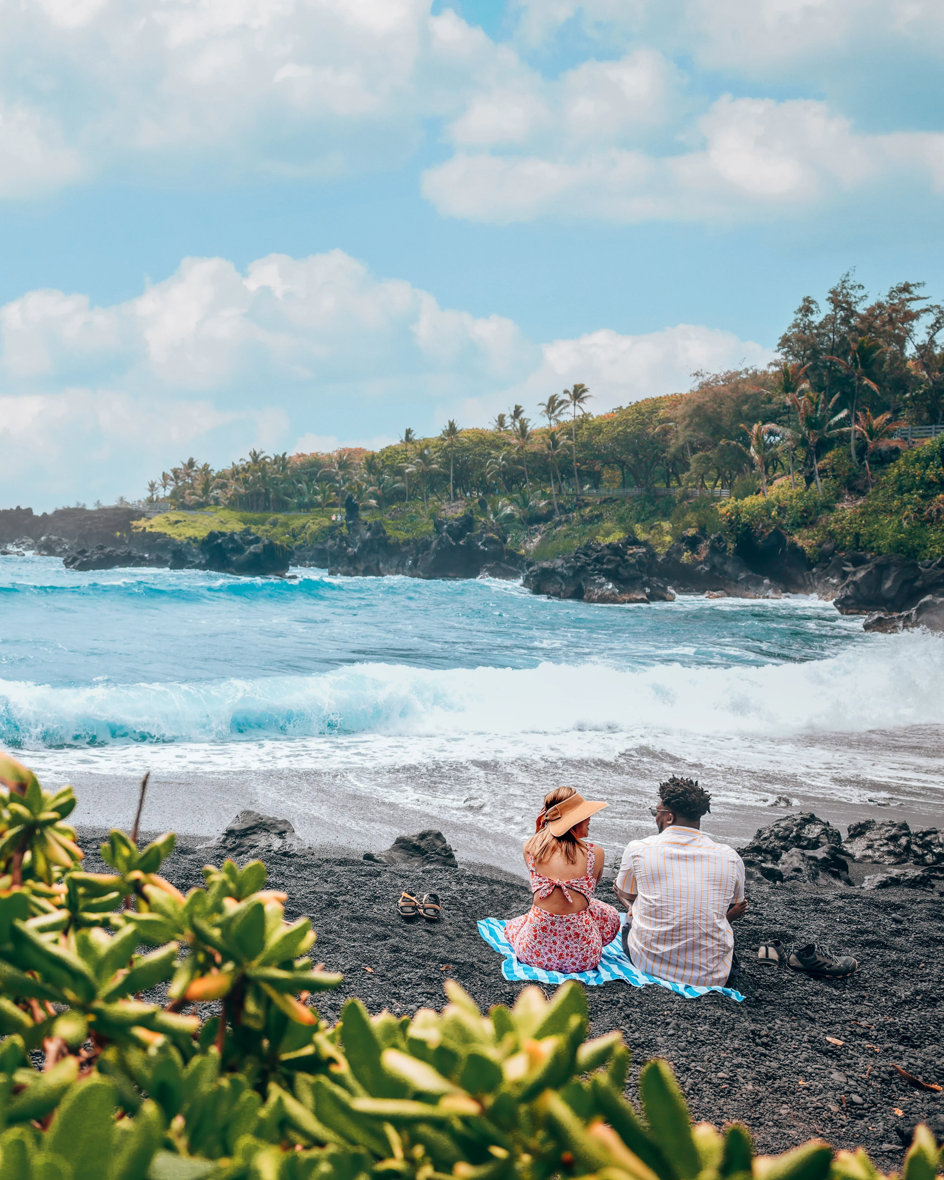 Couple sitting on black sand beach in Maui, Hawaii