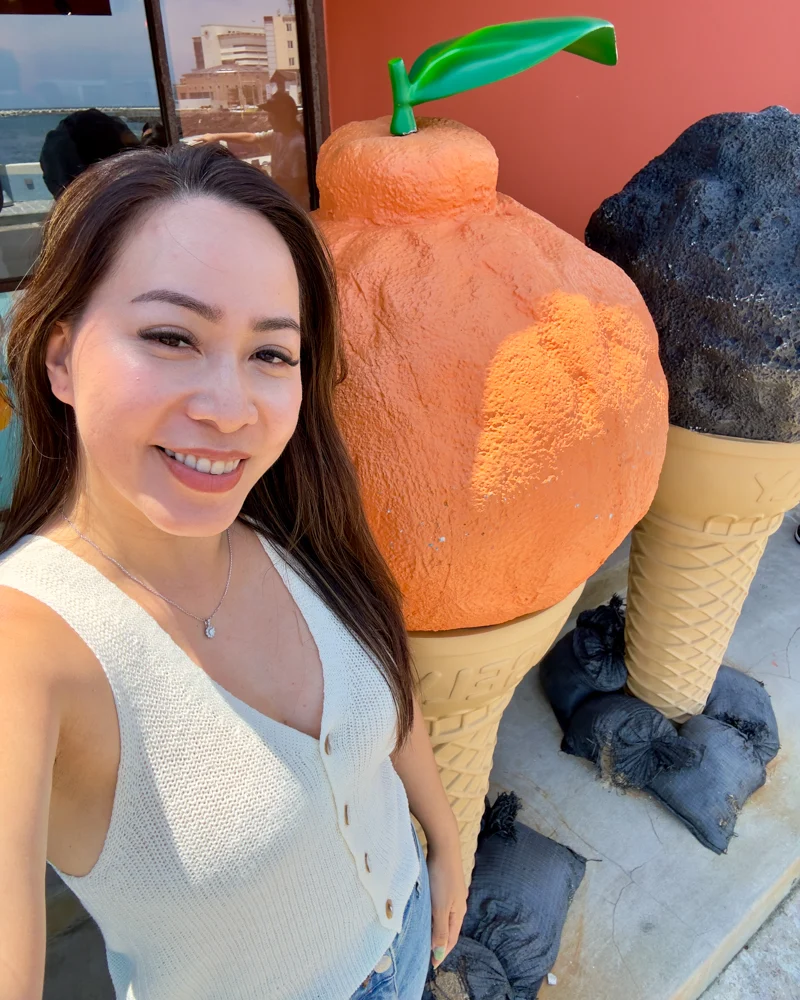 Woman standing next to giant ice-cream cones shaped like Hallabong and volcano on Jeju Island